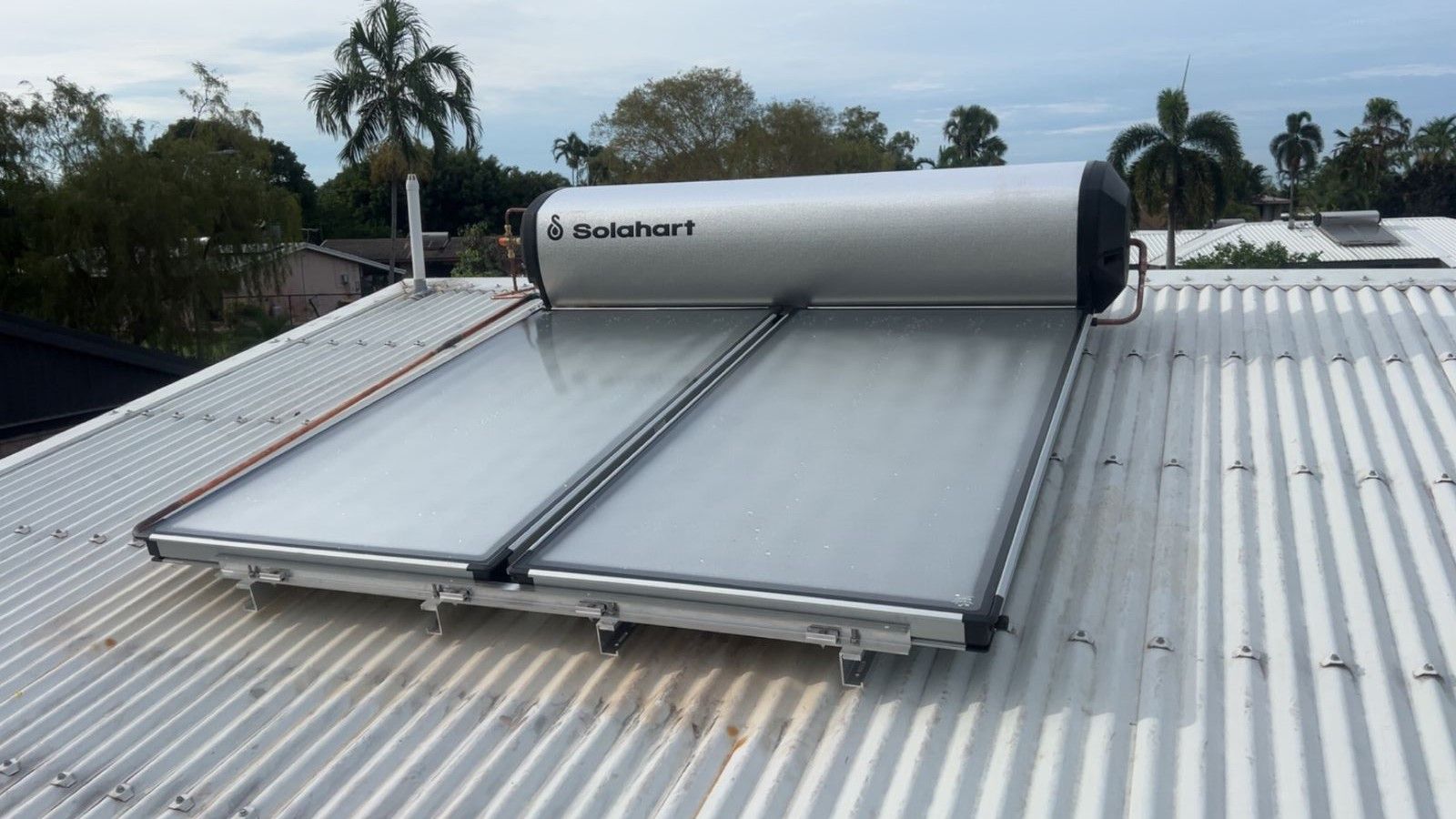 Solar water heater on a corrugated metal roof, with two flat panels and a silver tank. — Nightcliff Plumbing & Gas In Coconut Grove, NT
