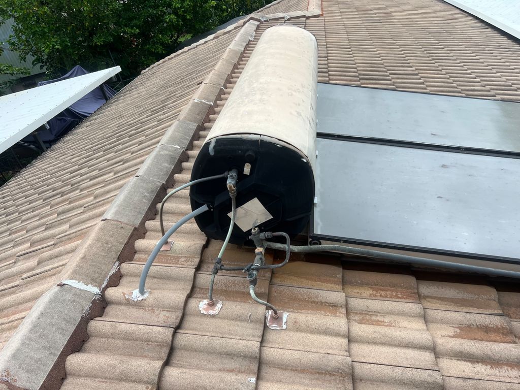 Solar water heater tank mounted on a tiled roof with visible pipes and wiring. — Nightcliff Plumbing & Gas In Coconut Grove, NT