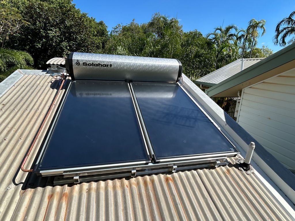 Solar water heater panels on a corrugated roof under a silver tank, with trees in the background — Nightcliff Plumbing & Gas In Coconut Grove, NT