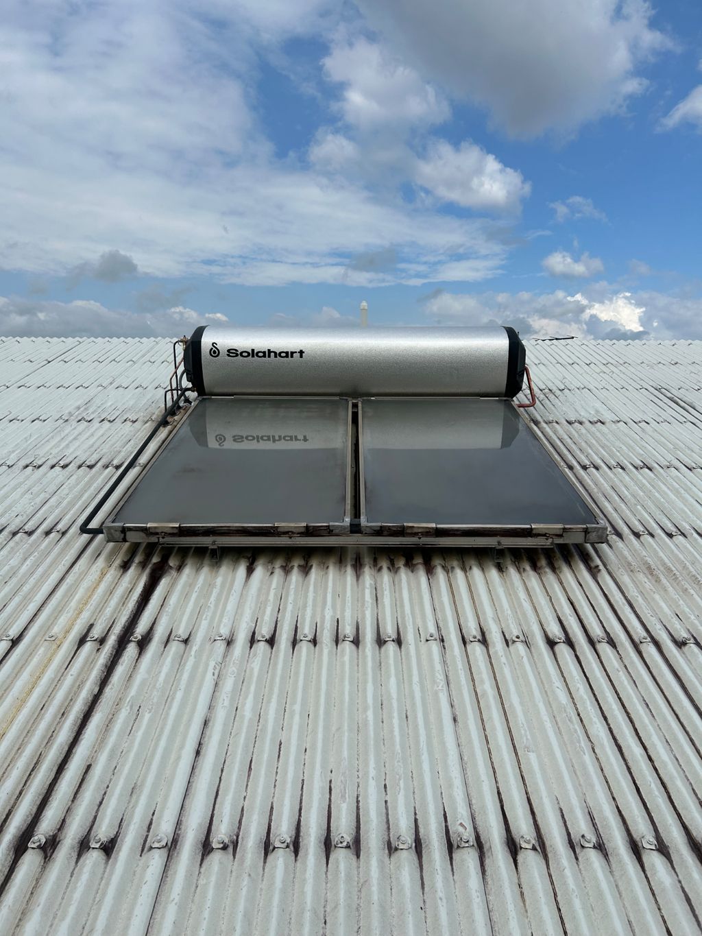 Rooftop solar water heater mounted on a corrugated metal roof under a cloudy sky — Nightcliff Plumbing & Gas In Coconut Grove, NT