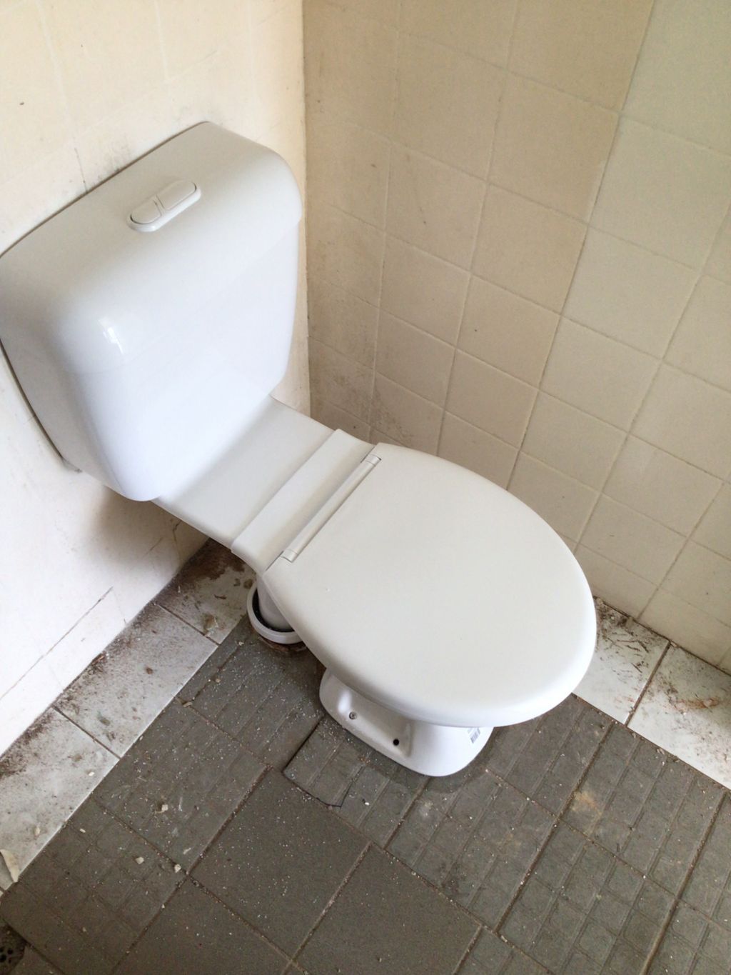 Small white toilet in a tiled bathroom corner with a gray tile — Nightcliff Plumbing & Gas In Fannie Bay, NT