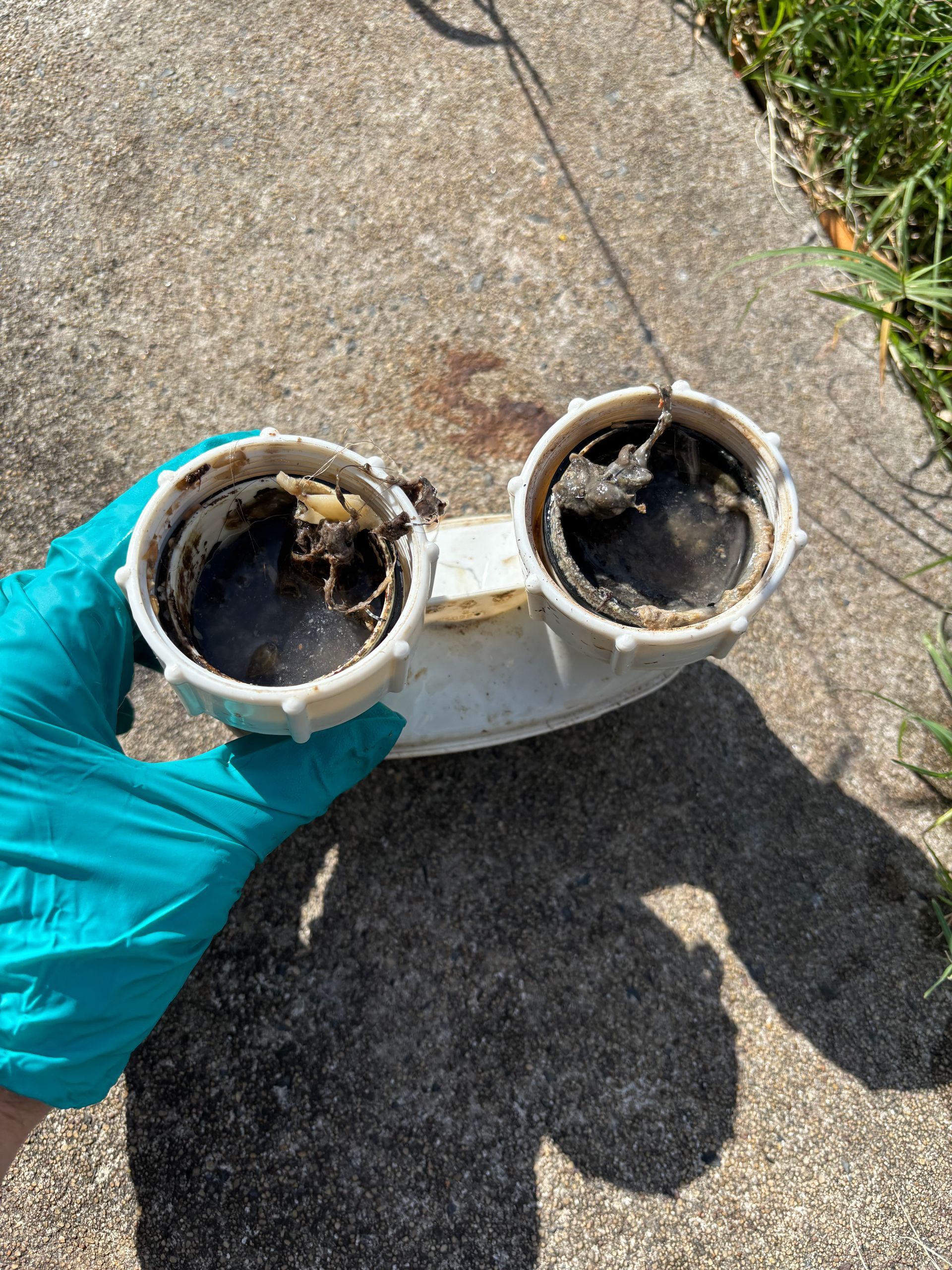Gloved hand holding two dirty, white PVC pipe fittings outdoors on pavement — Nightcliff Plumbing & Gas In Coconut Grove, NT