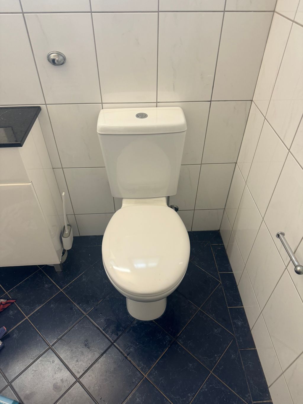 White toilet in a small tiled restroom with a dark blue floor and partial sink visible — Nightcliff Plumbing & Gas In Adelaide River, NT