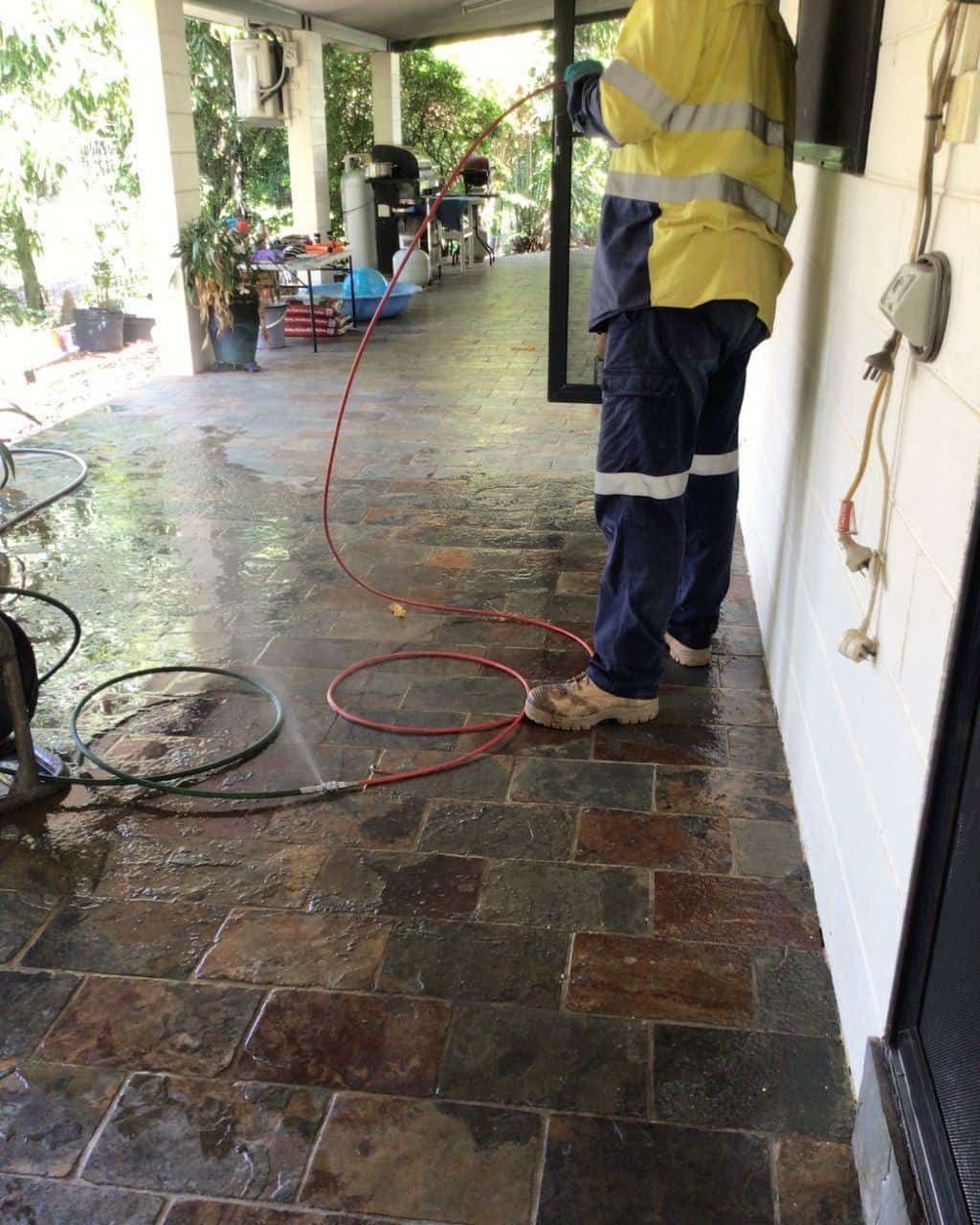 A Man is Cleaning a Tiled Floor With a Hose — Nightcliff Plumbing & Gas In Coconut Grove, NT