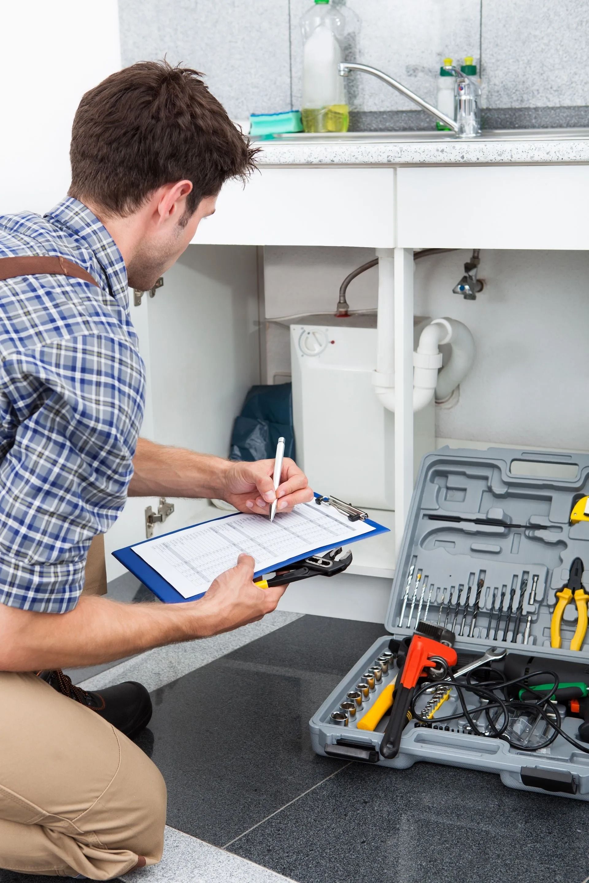 A Plumber is Kneeling Down in Front of a Sink and Writing on a Clipboard — Nightcliff Plumbing & Gas In Coconut Grove, NT