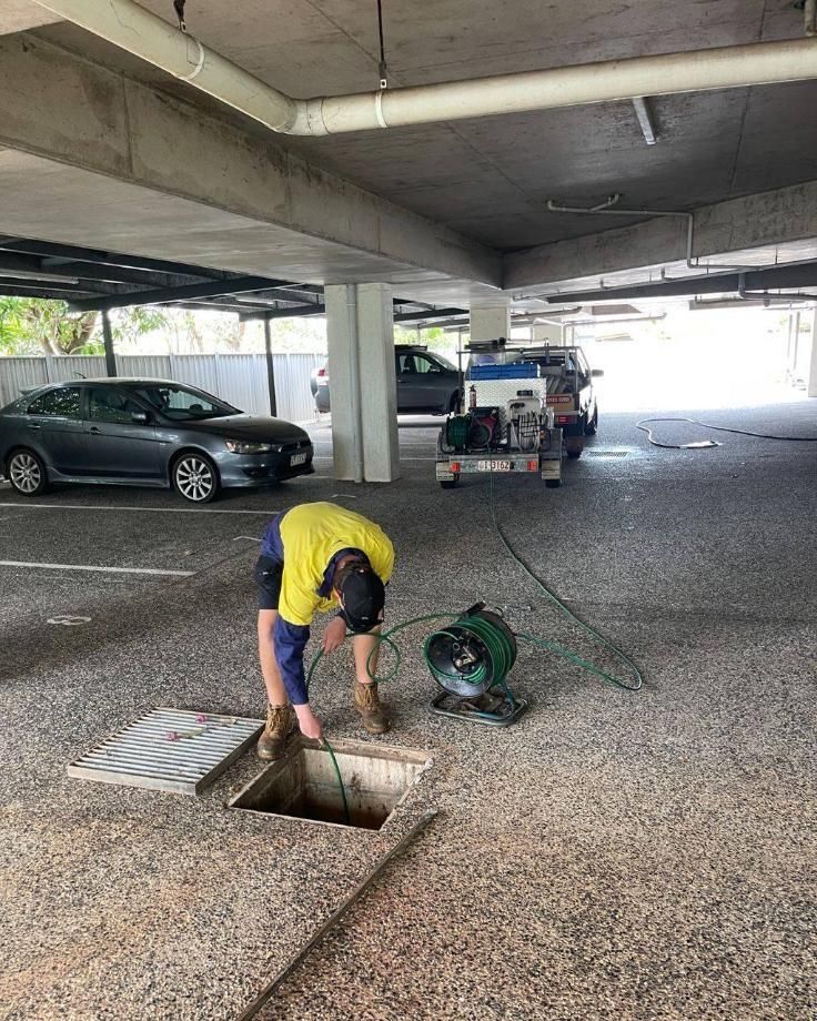 A Man is Working on a Drain in a Parking Garage — Nightcliff Plumbing & Gas In Stuart Park, NT