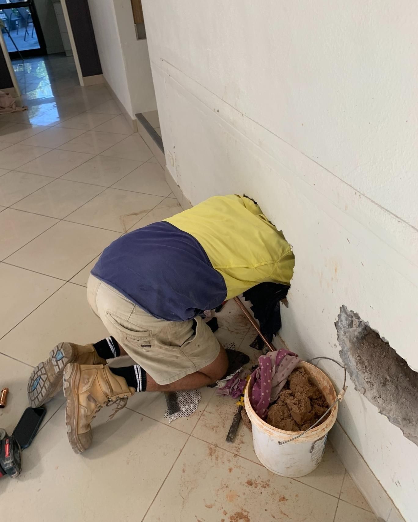 A Man is Kneeling Down Next to a Bucket of Dirt — Nightcliff Plumbing & Gas In Parap, NT
