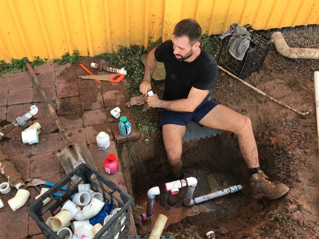 A Man is Sitting in the Dirt Working on a Pipe — Nightcliff Plumbing & Gas In Palmerston, NT