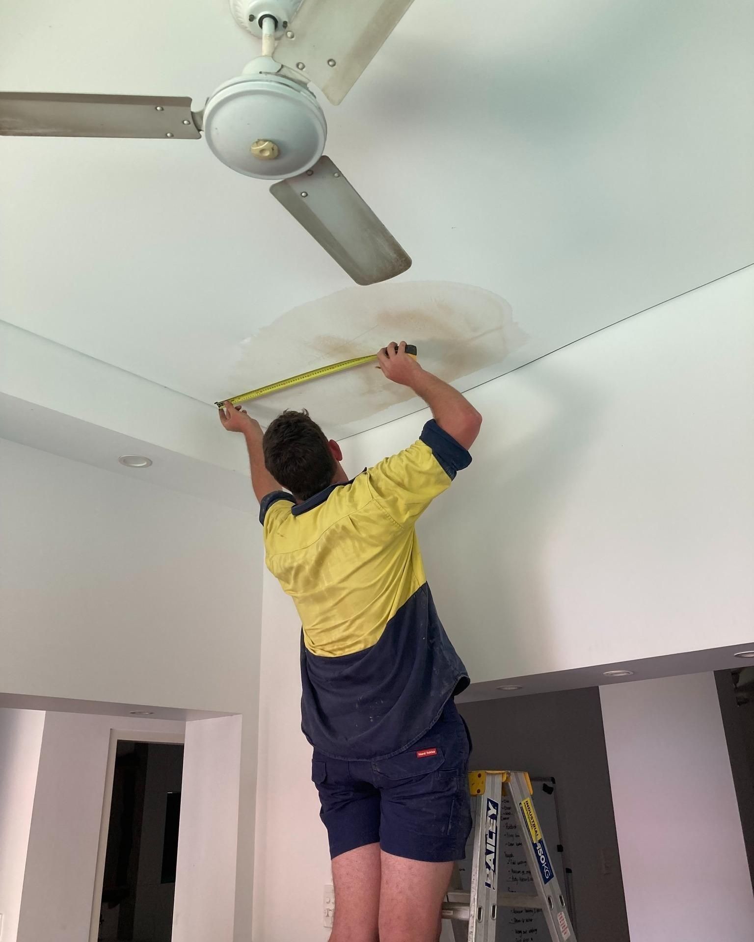 A Man is Measuring the Ceiling With a Tape Measure — Nightcliff Plumbing & Gas In Leanyer, NT