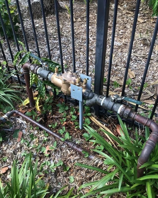 A Water Valve is Sitting in the Middle of a Garden Next to a Fence — Nightcliff Plumbing & Gas In Coconut Grove, NT