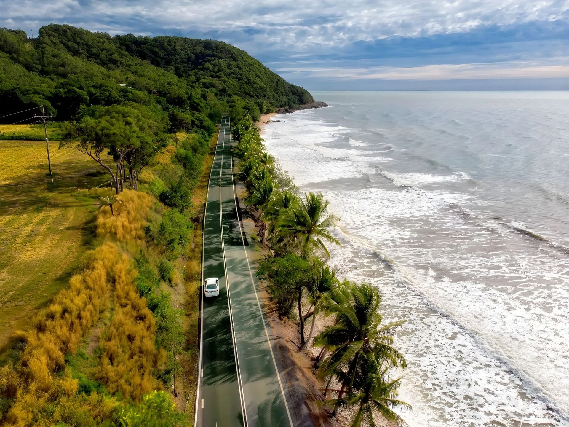 A Car is Driving Down a Road Next to the Ocean — Nightcliff Plumbing & Gas In Coconut Grove, NT