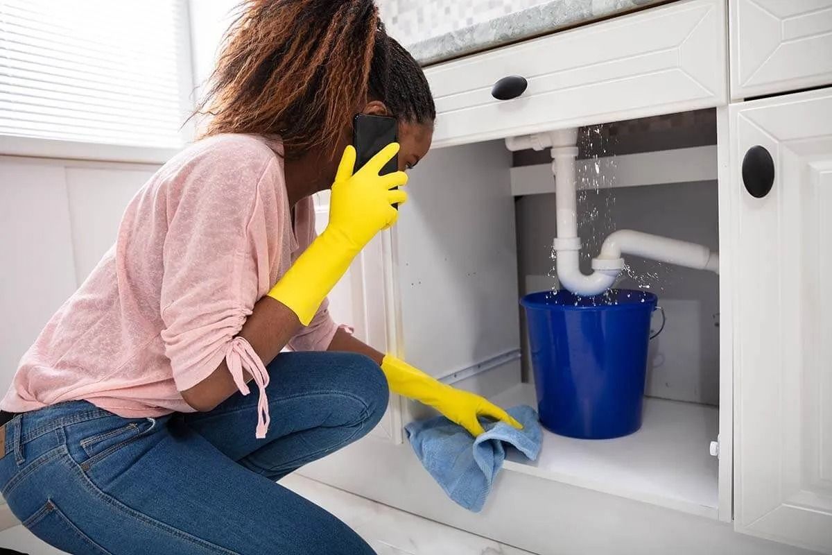 A Woman is Kneeling Under a Sink Talking on a Cell Phone — Nightcliff Plumbing & Gas In Coconut Grove, NT