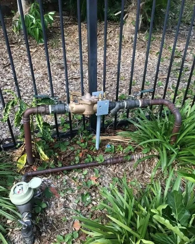 A Water Meter is Sitting on the Ground Next to a Fence — Nightcliff Plumbing & Gas In Coconut Grove, NT