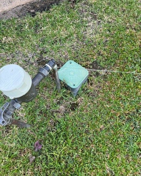 A Water Meter is Sitting in the Grass Next to a Green Box — Nightcliff Plumbing & Gas In Leanyer, NT
