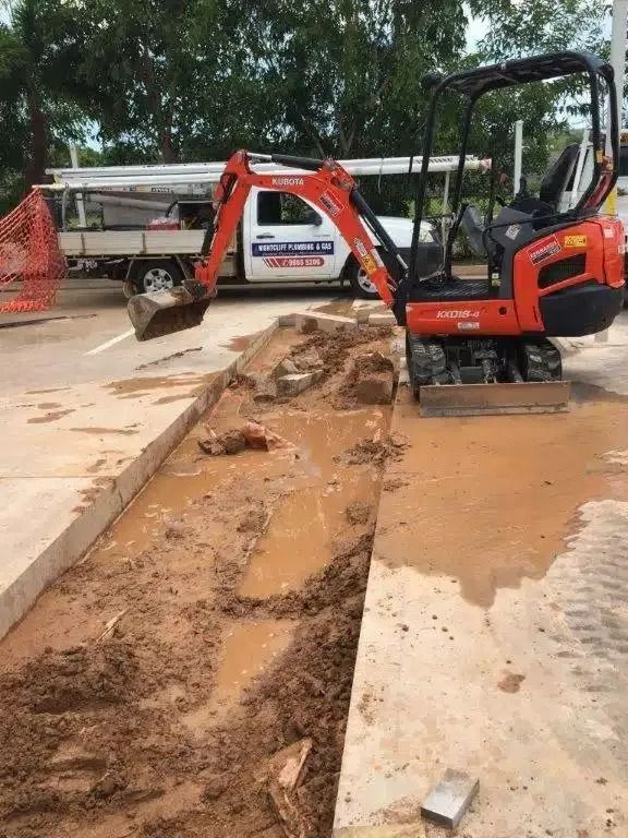 A Small Orange Excavator is Digging a Hole in the Ground — Nightcliff Plumbing & Gas In Coconut Grove, NT