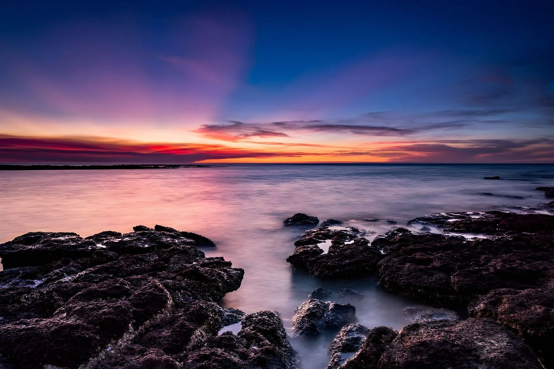 A Sunset Over the Ocean With Rocks — Nightcliff Plumbing & Gas In Nightcliff, NT