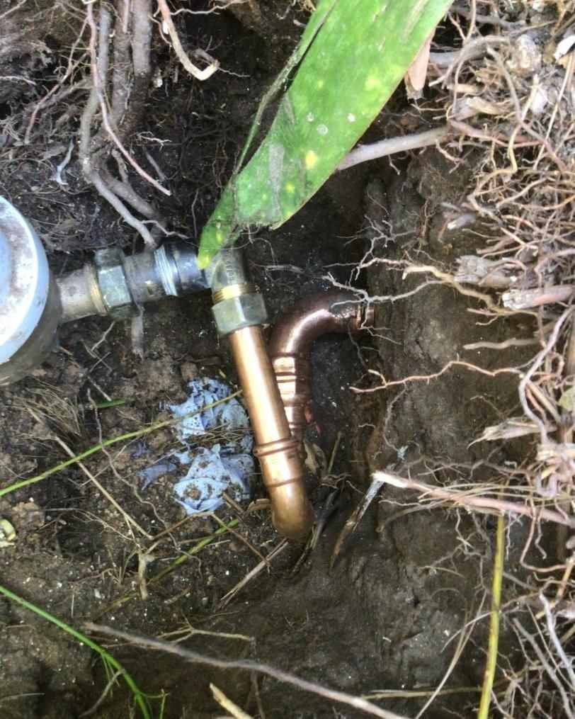 A Copper Pipe is Laying in the Dirt Next to a Plant — Nightcliff Plumbing & Gas In Coconut Grove, NT