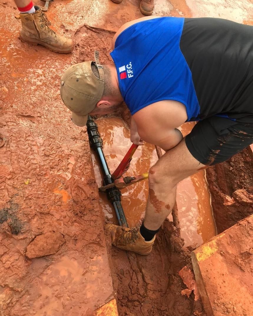 A Man is Fixing A Pipe In A Muddy Trench— Nightcliff Plumbing & Gas In Adelaide River, NT