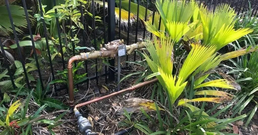 Copper Pipe is Sitting in the Middle of a Garden Next to a Fence — Nightcliff Plumbing & Gas In Coconut Grove, NT