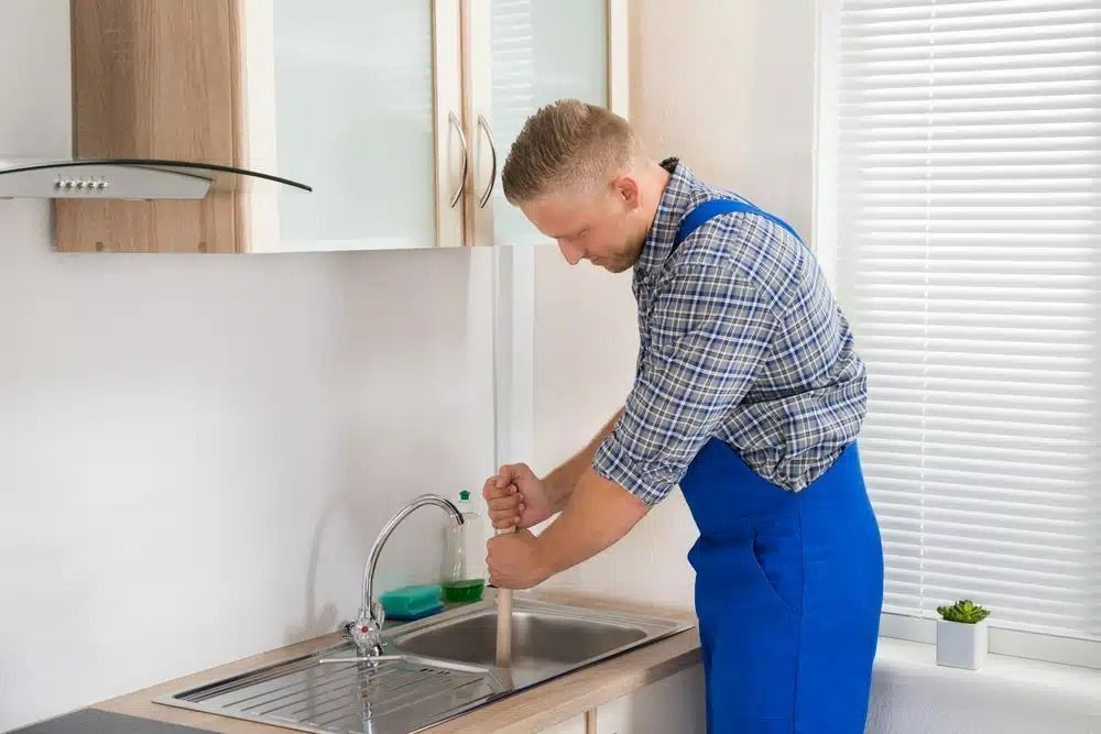 A Man is Cleaning a Kitchen Sink With a Plunger — Nightcliff Plumbing & Gas In Coconut Grove, NT