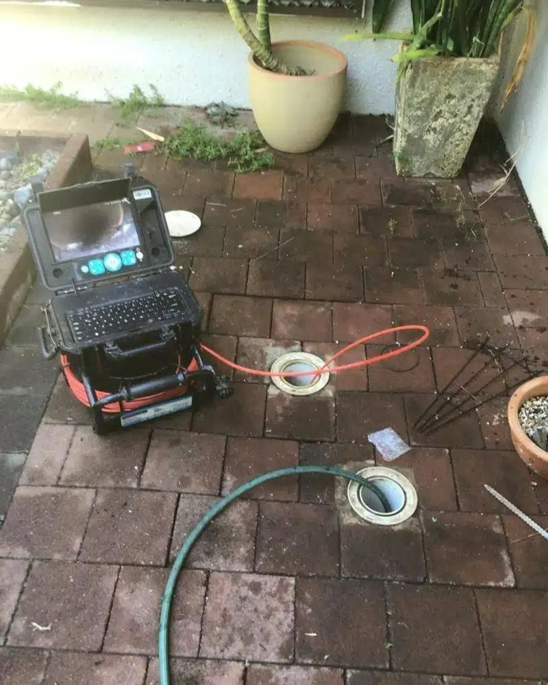 A Camera is Sitting on a Brick Floor Next to a Hose — Nightcliff Plumbing & Gas In Coconut Grove, NT