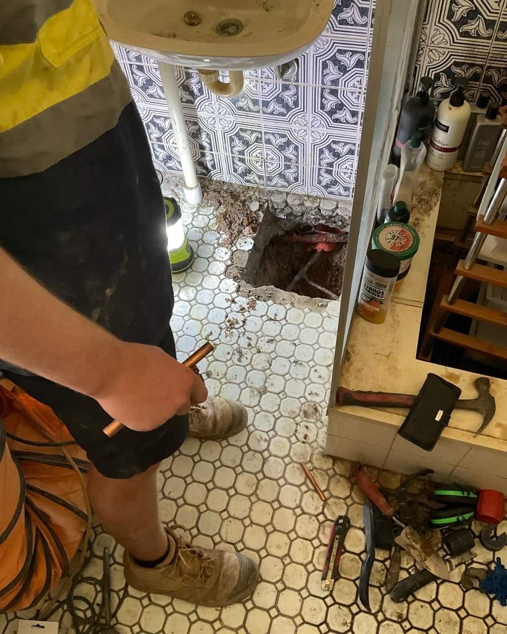 A Man is Standing in a Bathroom Next to a Sink and a Hole in the Floor — Nightcliff Plumbing & Gas In Coconut Grove, NT