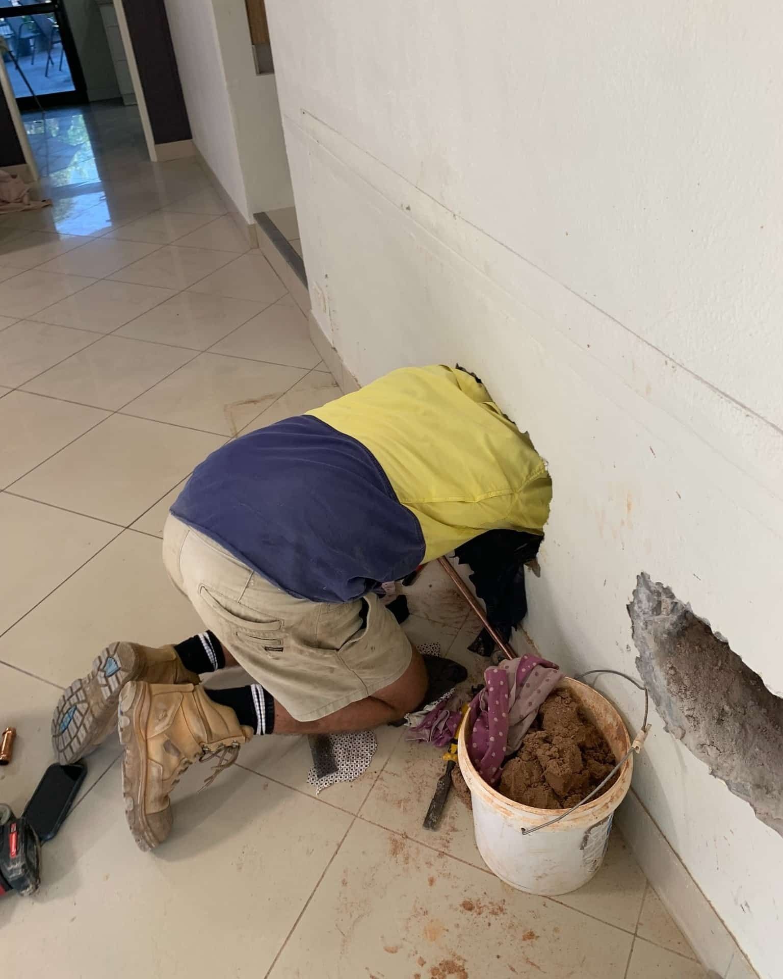 A Man is Kneeling Down Next to a Bucket of Dirt — Nightcliff Plumbing & Gas In Coconut Grove, NT