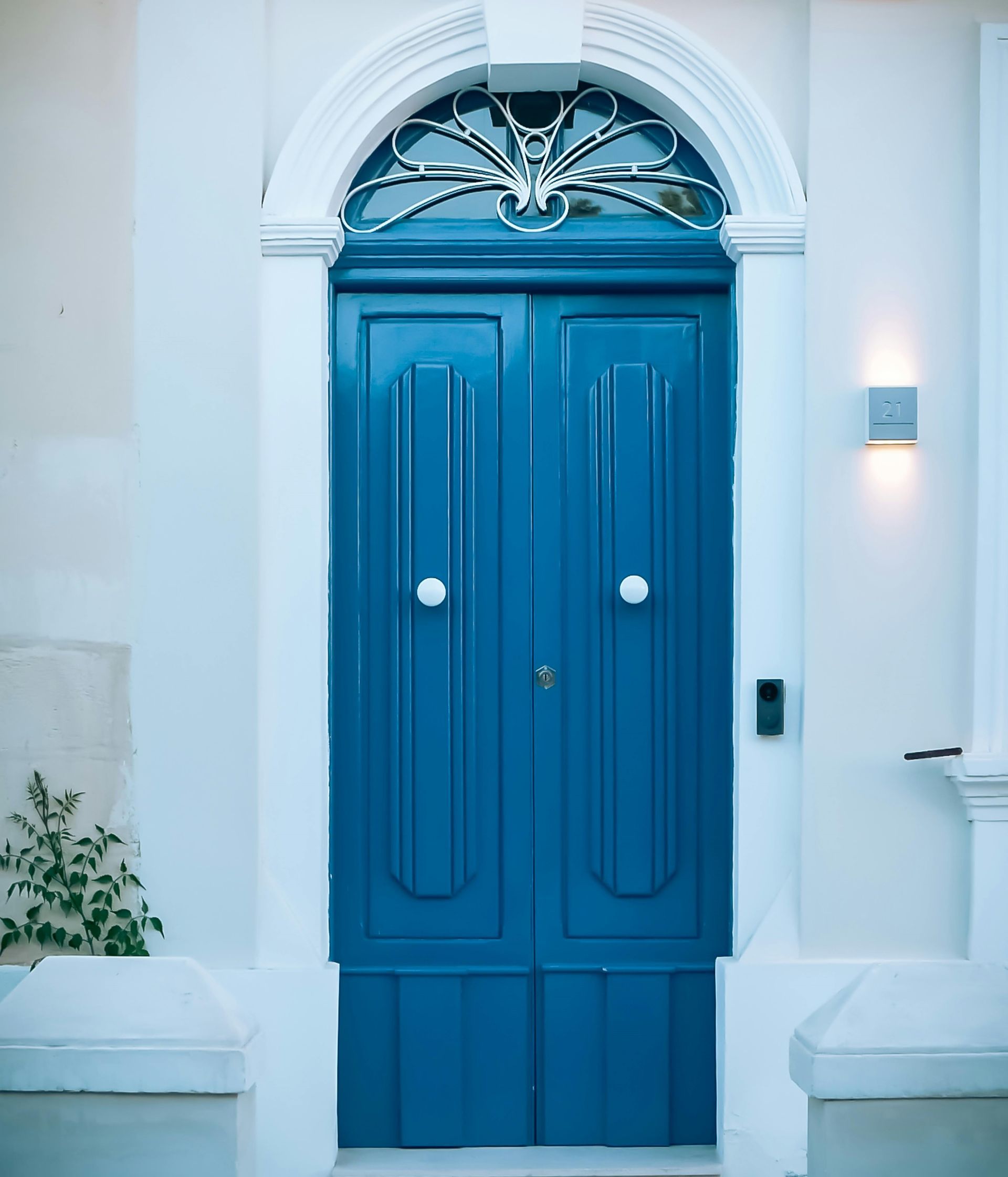 Blue double front door with white trim and decorative archway on a white building