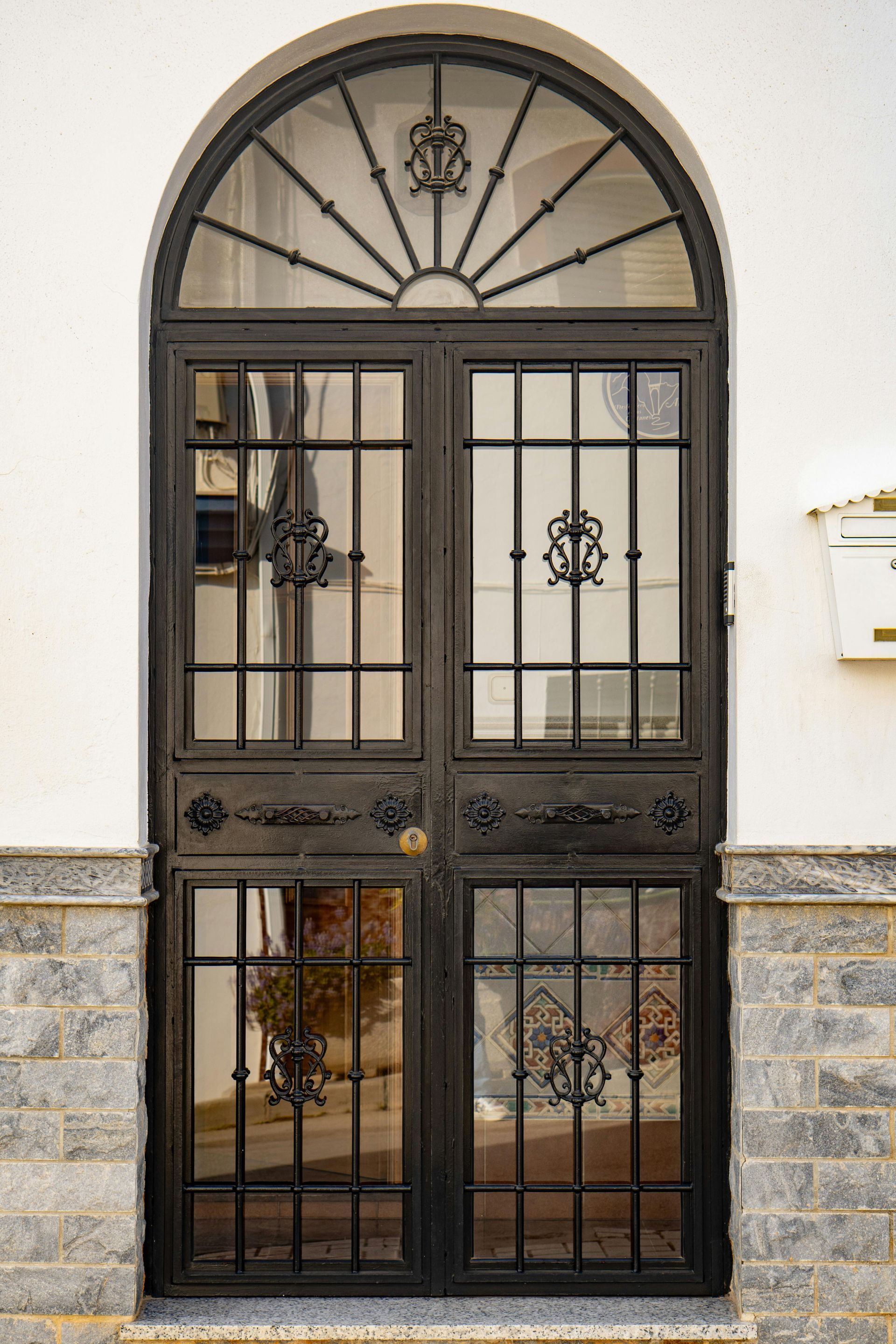 Black wrought-iron door with an arched transom in a Redwood City stone building entrance