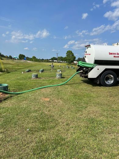 A septic tank truck is pumping water into a field.