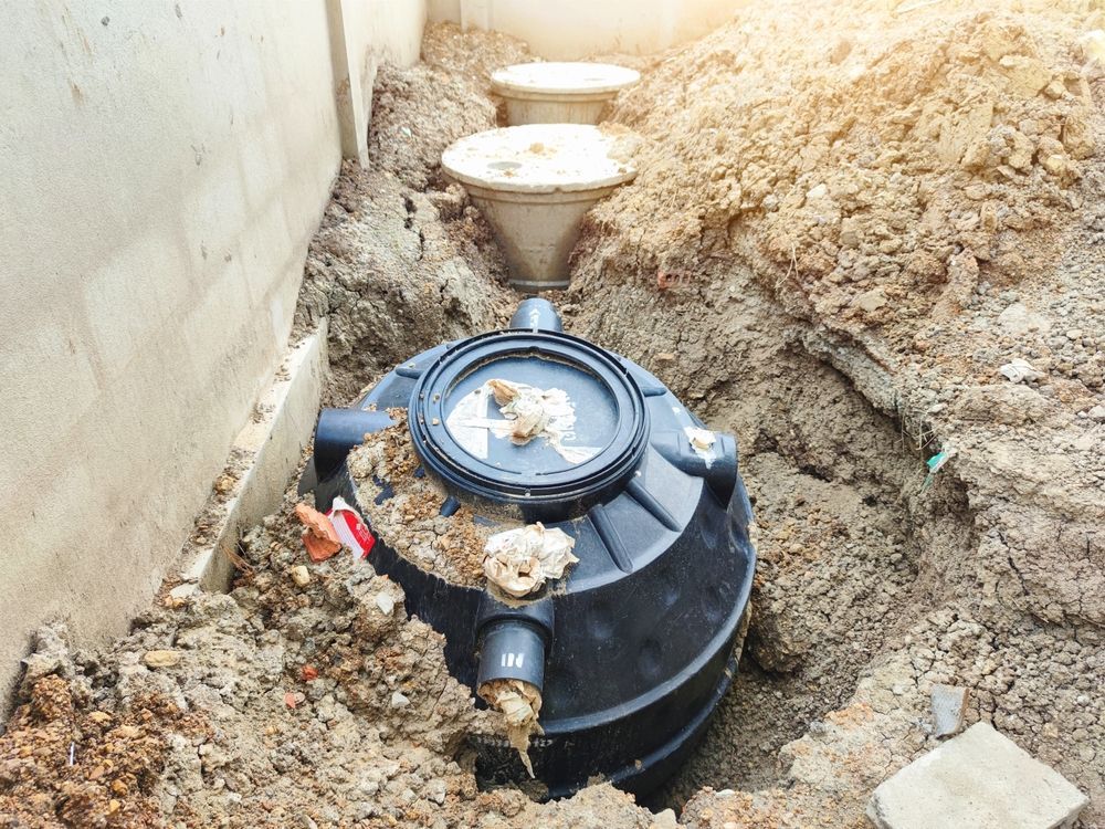 A septic tank is sitting in the dirt next to a wall.