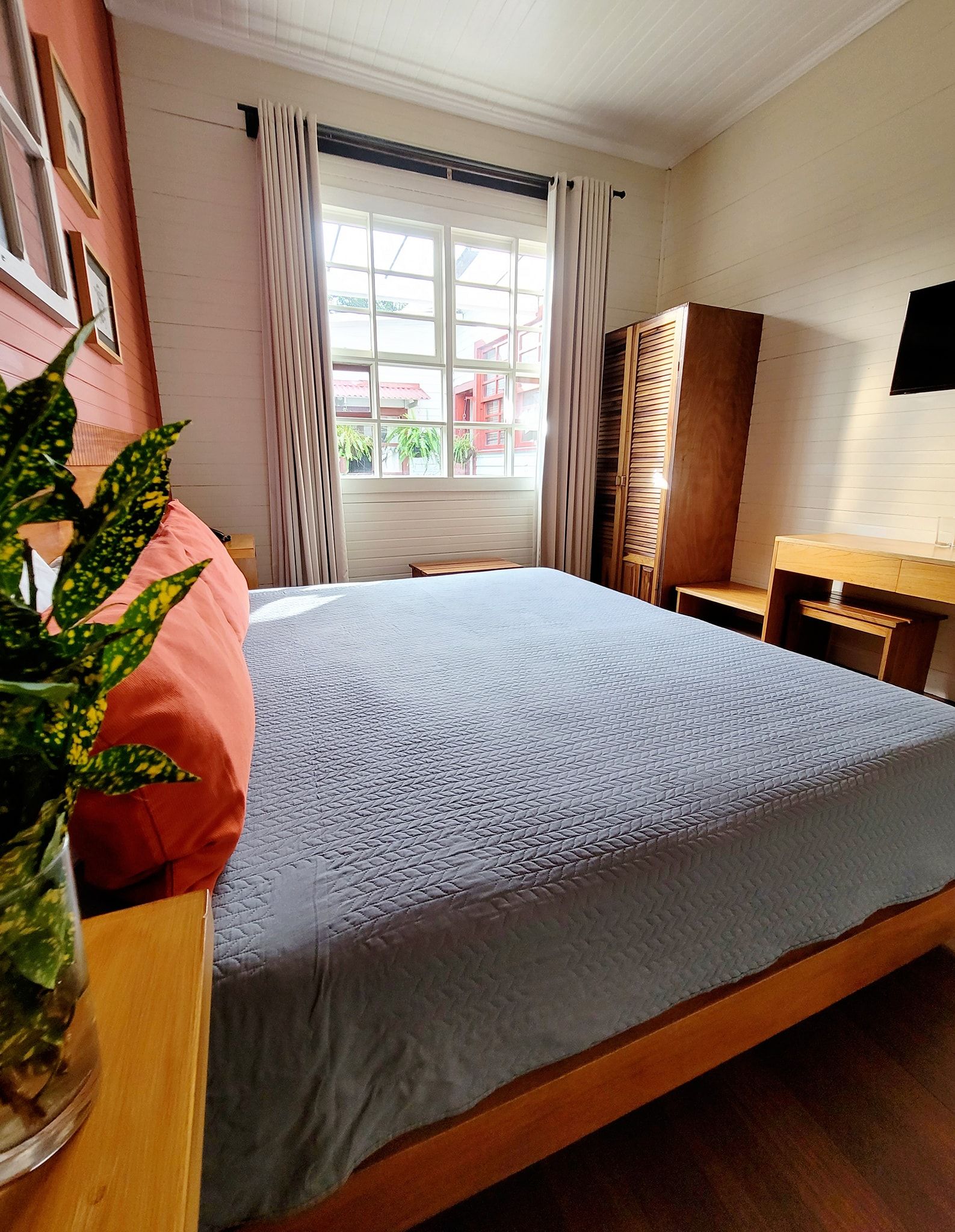 Bright bedroom with a large bed, window, curtains, and a small desk by the wall.