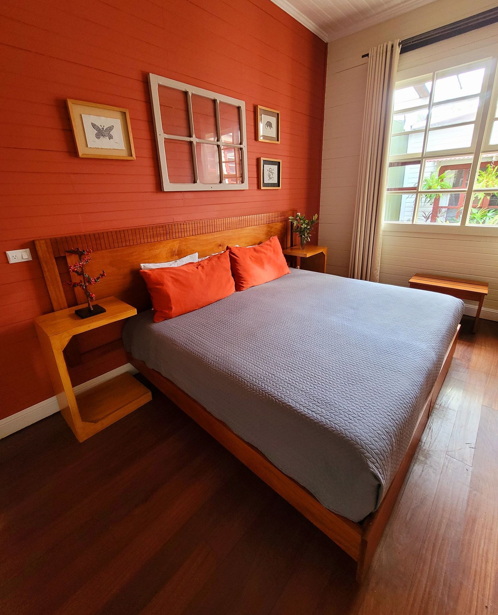 Bright cozy bedroom with a wooden bed, orange walls, gray bedspread, and a sunlit window