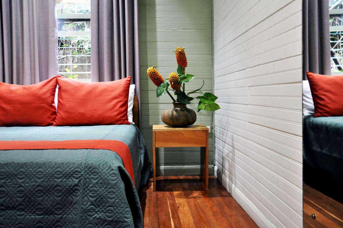 Cozy bedroom with two beds, red pillows, wood floor, and a small table with flowers between them