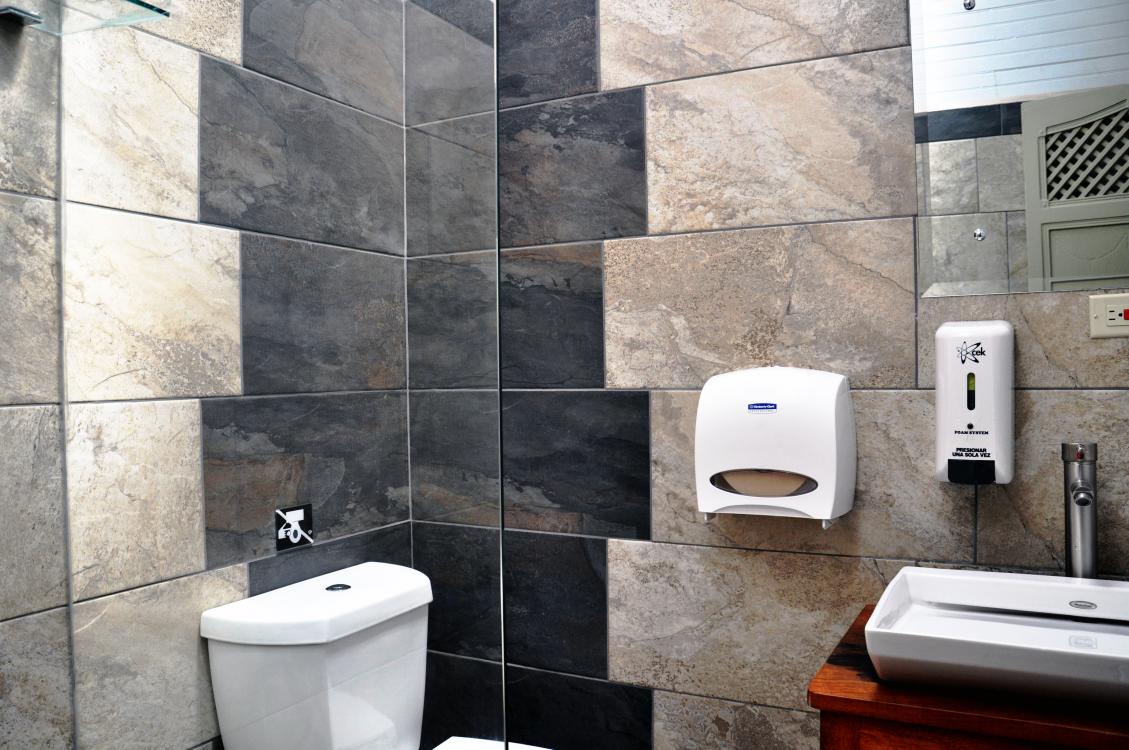 Public restroom with tiled walls, toilet, sink, soap dispenser, and paper towel dispenser.