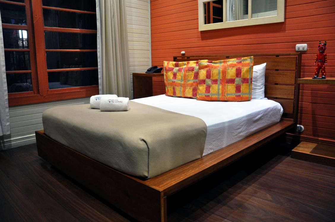 Modern bedroom with a wooden bed, gray blanket, colorful pillows, and dark wood flooring