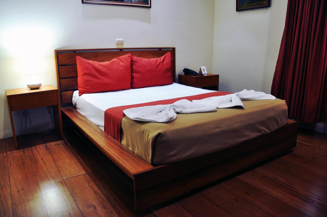Wooden bed with red pillows and white bedding in a cozy bedroom with dark curtains and wood floors