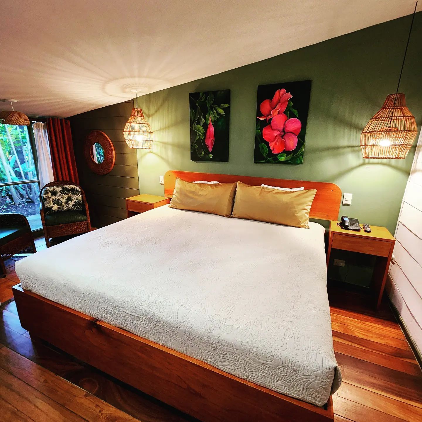 Cozy bedroom with large white bed, warm wood floors, green walls, floral art, and hanging lamps