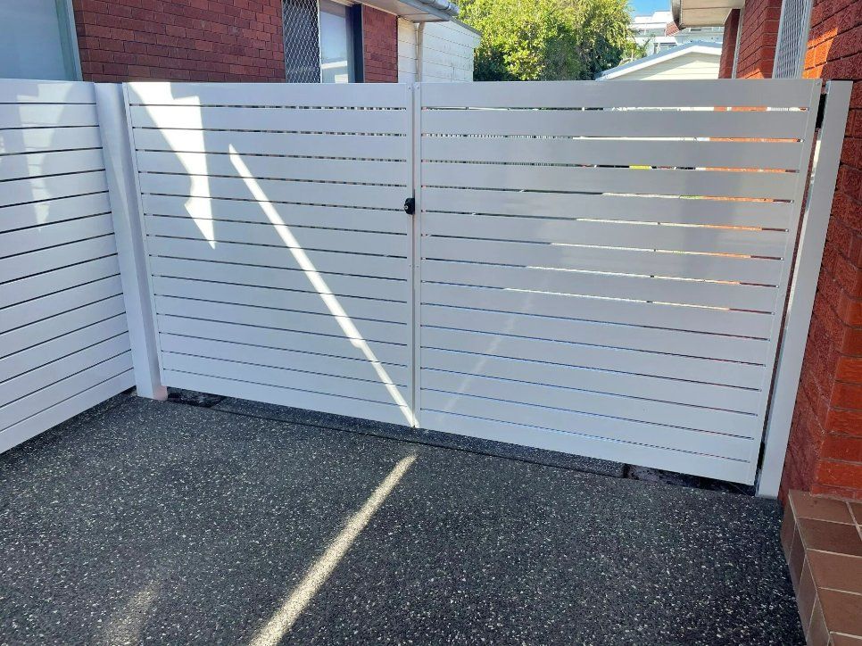 A White Fence Is Sitting in Front of A Brick Building — Topline Aluminium Forster Pty Ltd in Forster, NSW