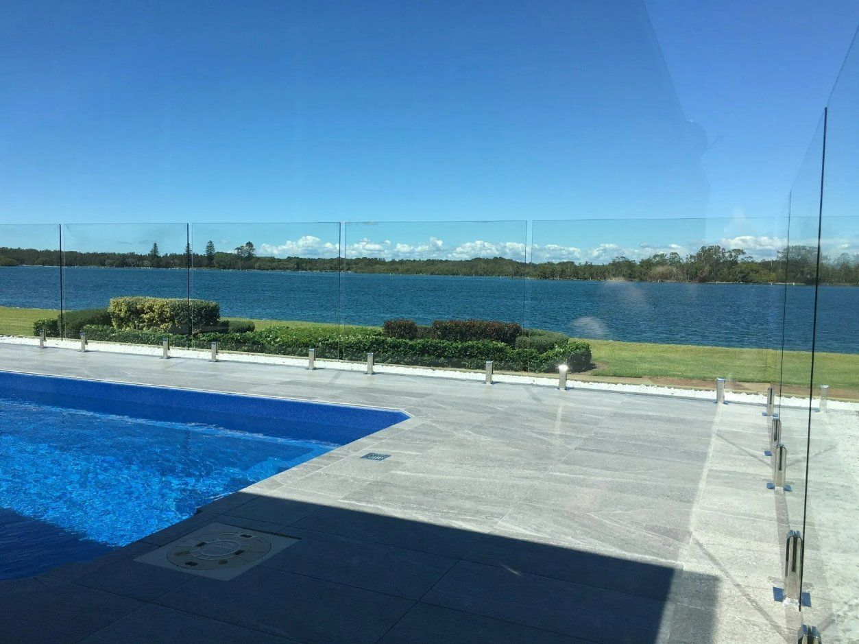 A Swimming Pool with A Glass Fence and A View of A Lake — Topline Aluminium Forster Pty Ltd in Forster, NSW