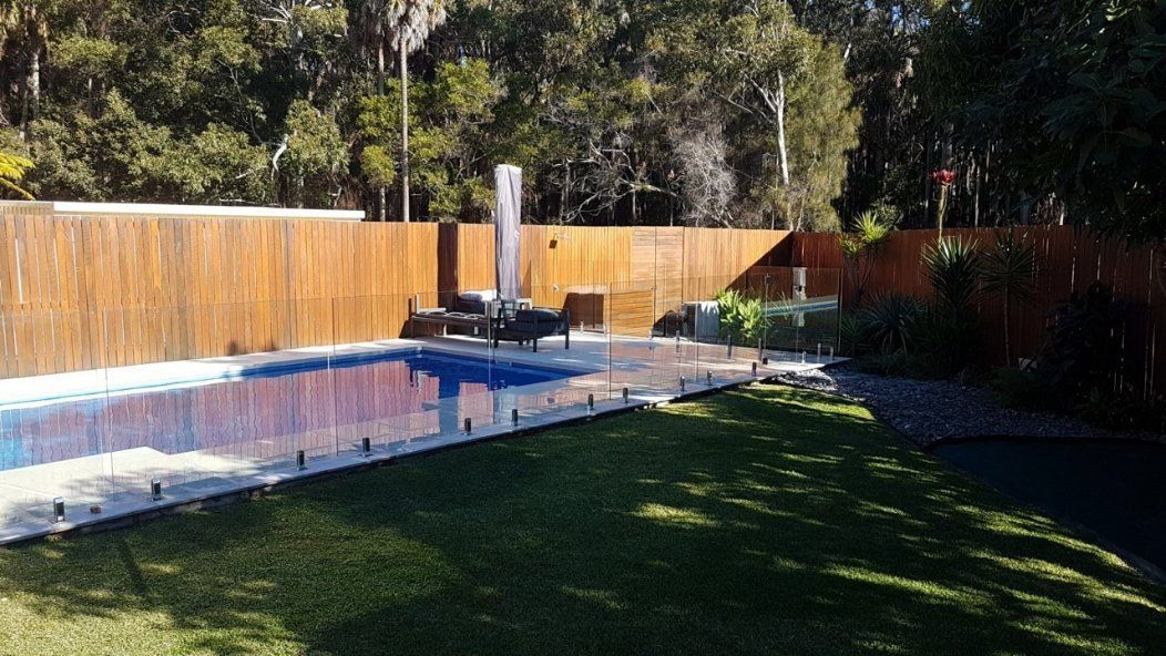 A Large Swimming Pool Is Surrounded by A Wooden Fence in A Backyard — Topline Aluminium Forster Pty Ltd in Smiths Lake, NSW