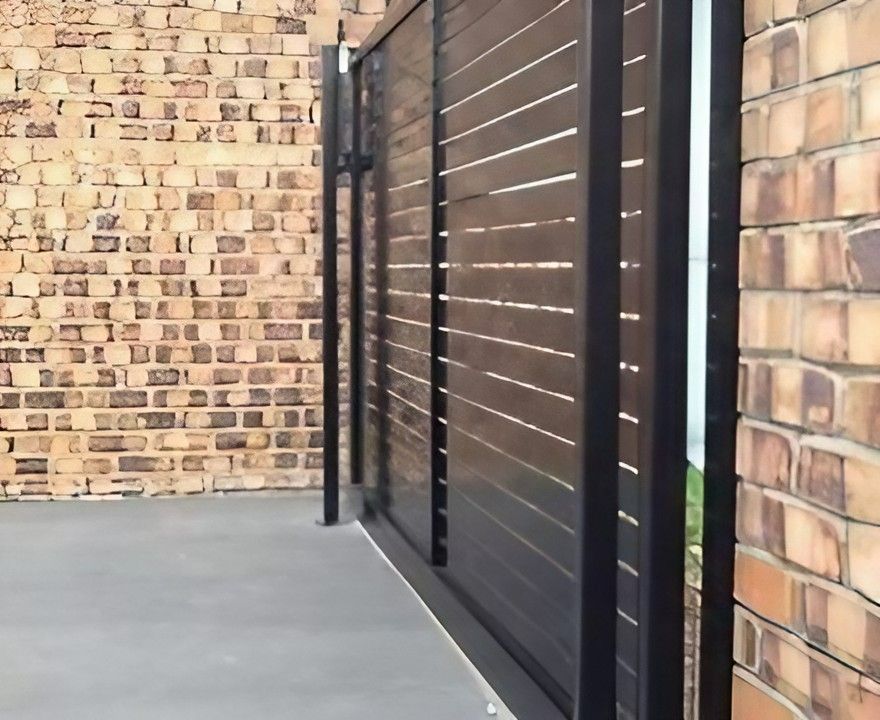A brick wall with a black fence in front of it — Topline Aluminium Forster Pty Ltd in Tuncurry, NSW