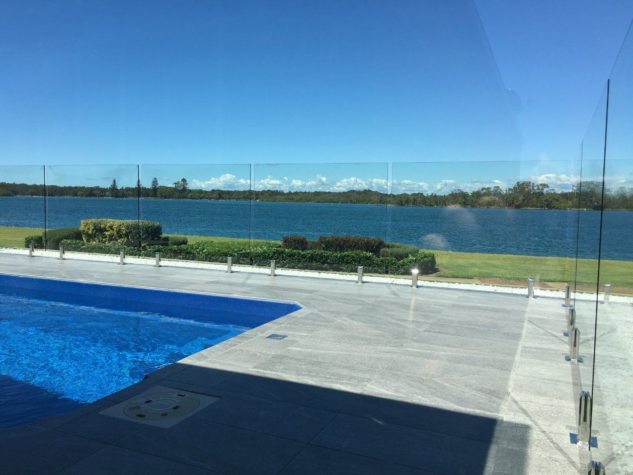 A Swimming Pool with A View of A Lake Behind a Glass Fence — Topline Aluminium Forster Pty Ltd in Tuncurry, NSW