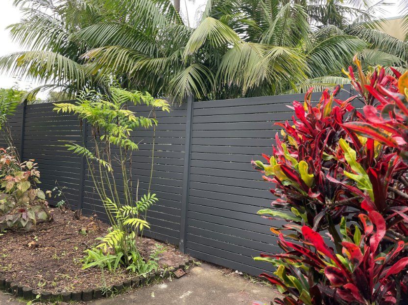 Black Fence Surrounds a Garden with Lots of Plants — Topline Aluminium Forster Pty Ltd in Tuncurry, NSW