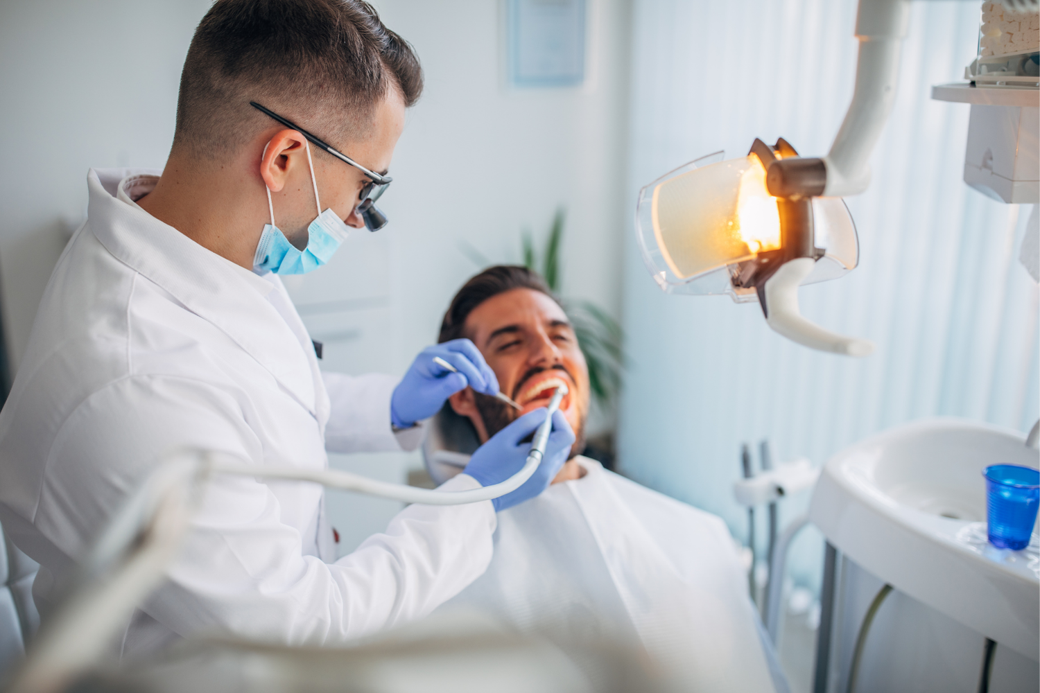 Dentist examining a smiling patient under a bright dental lamp in a clinic