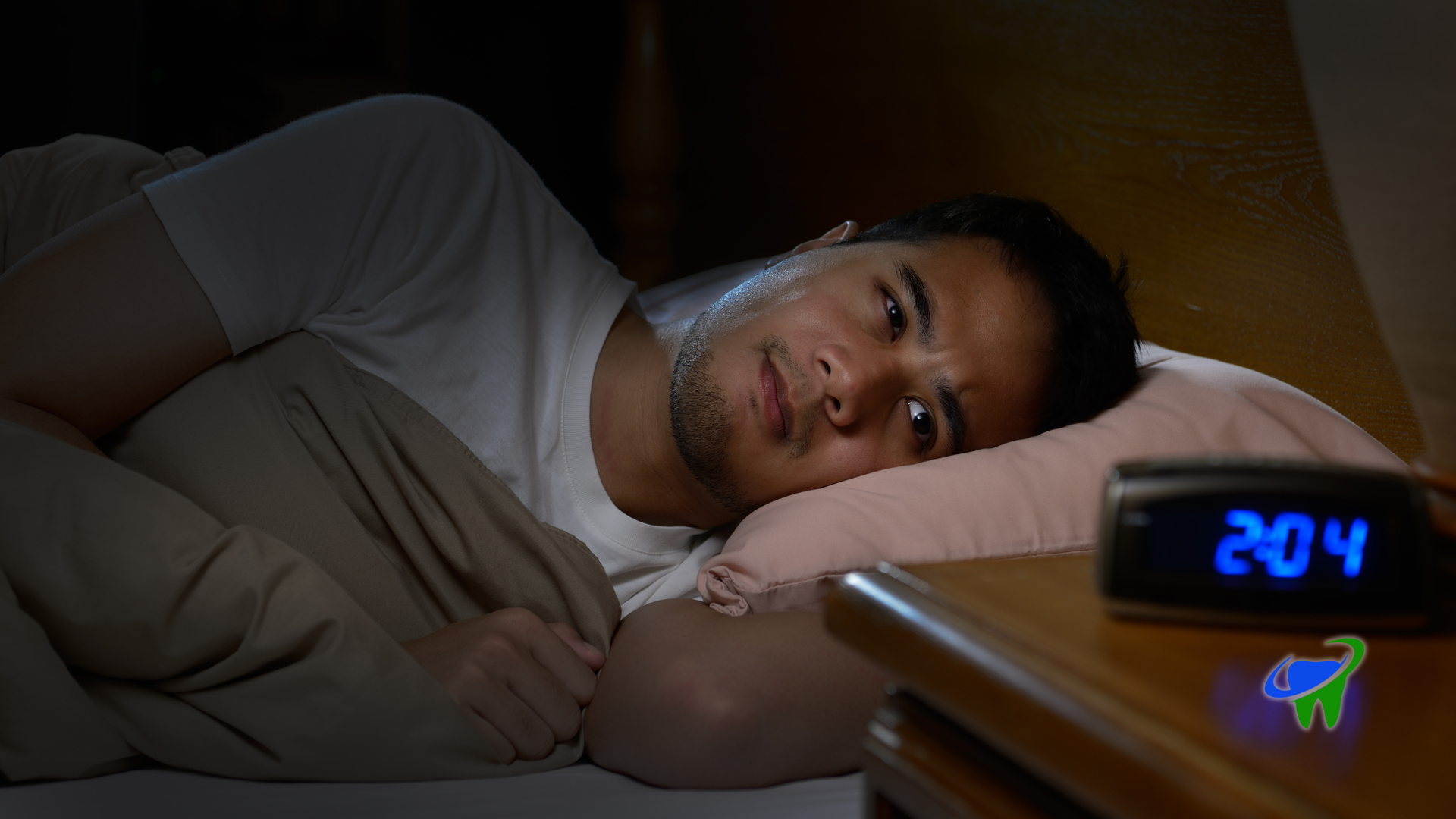 Person lying in bed at night beside a glowing digital clock reading 2:04