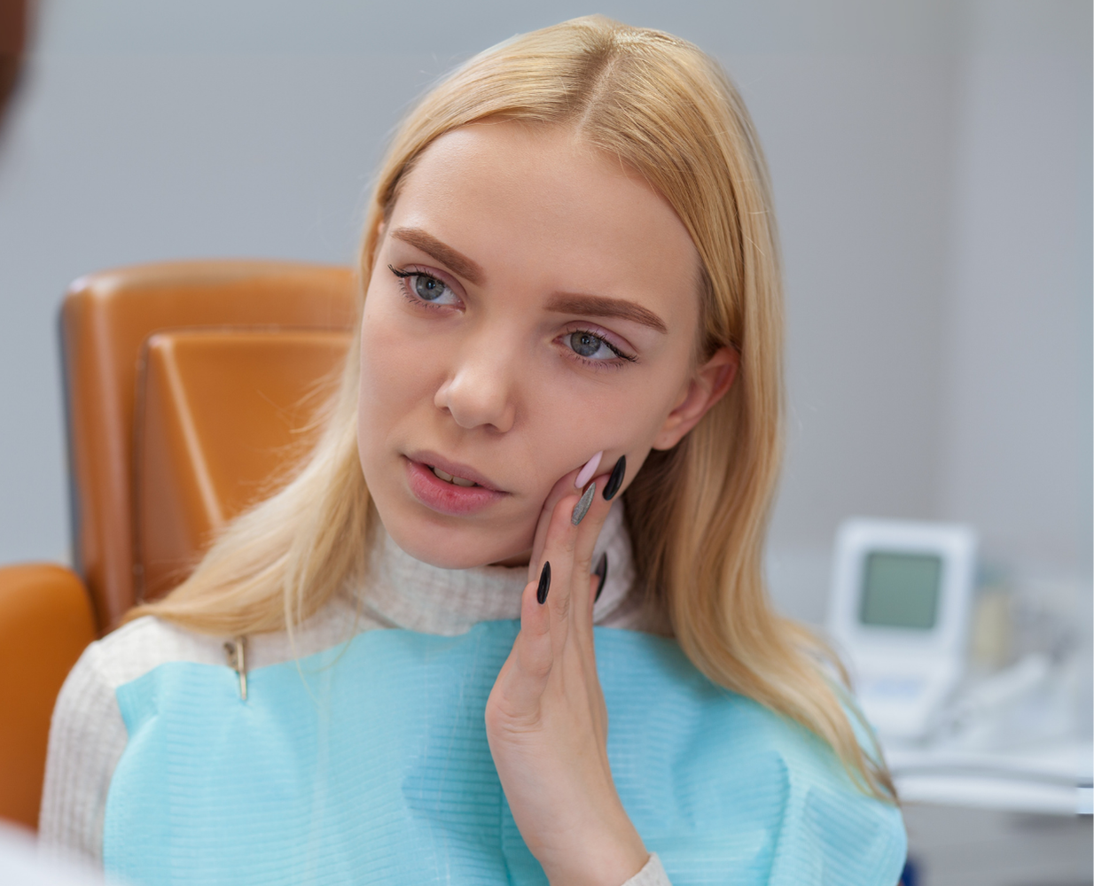 Blonde woman in a blue top touching her cheek in a dental clinic waiting area