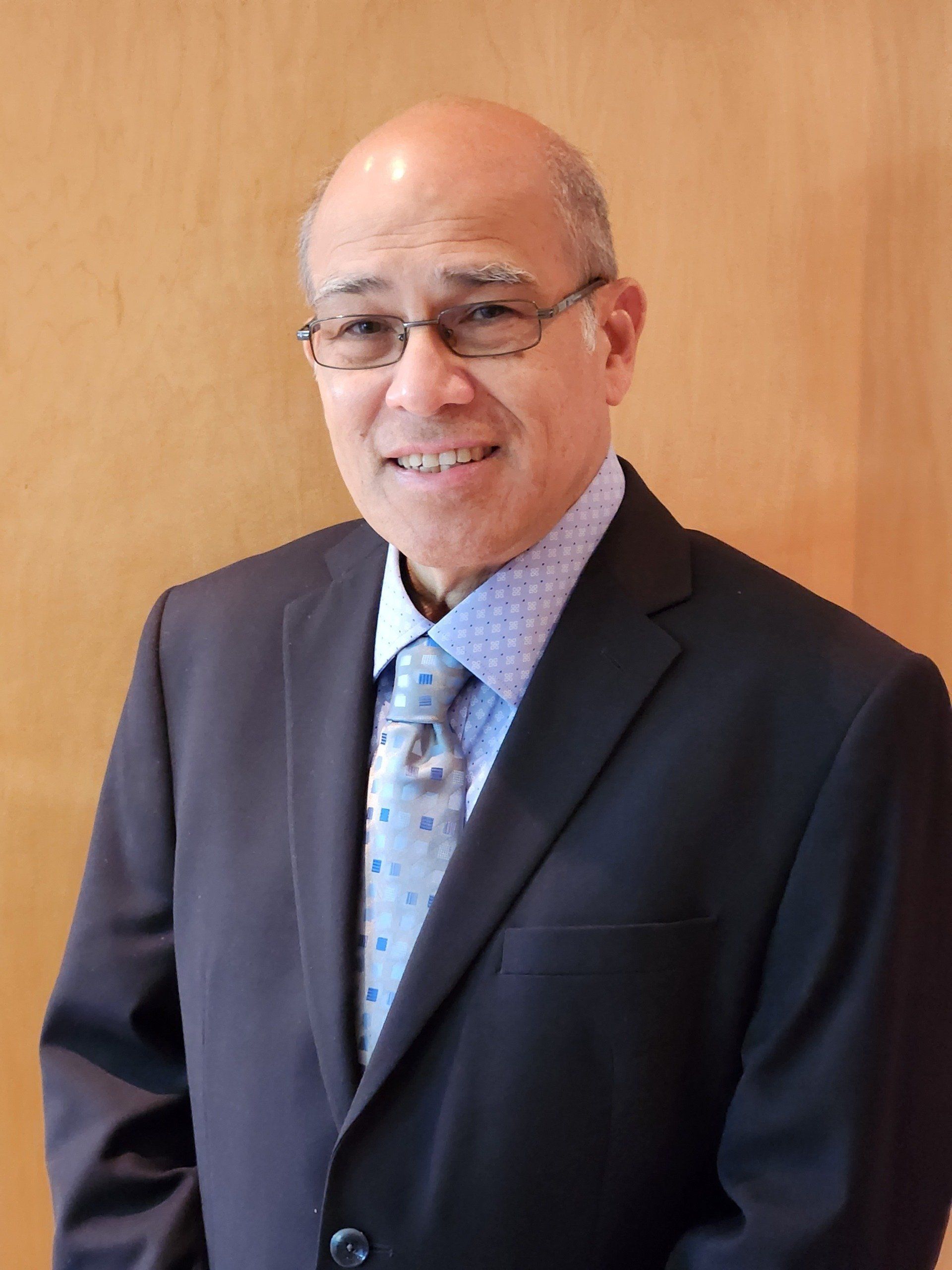 A man in a suit and tie is standing in front of a wooden wall.