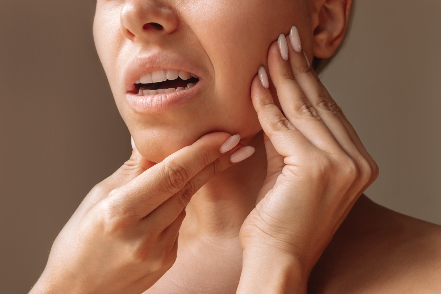 Hands touching a person’s jaw and neck, highlighting lower face pain or skin care concern.