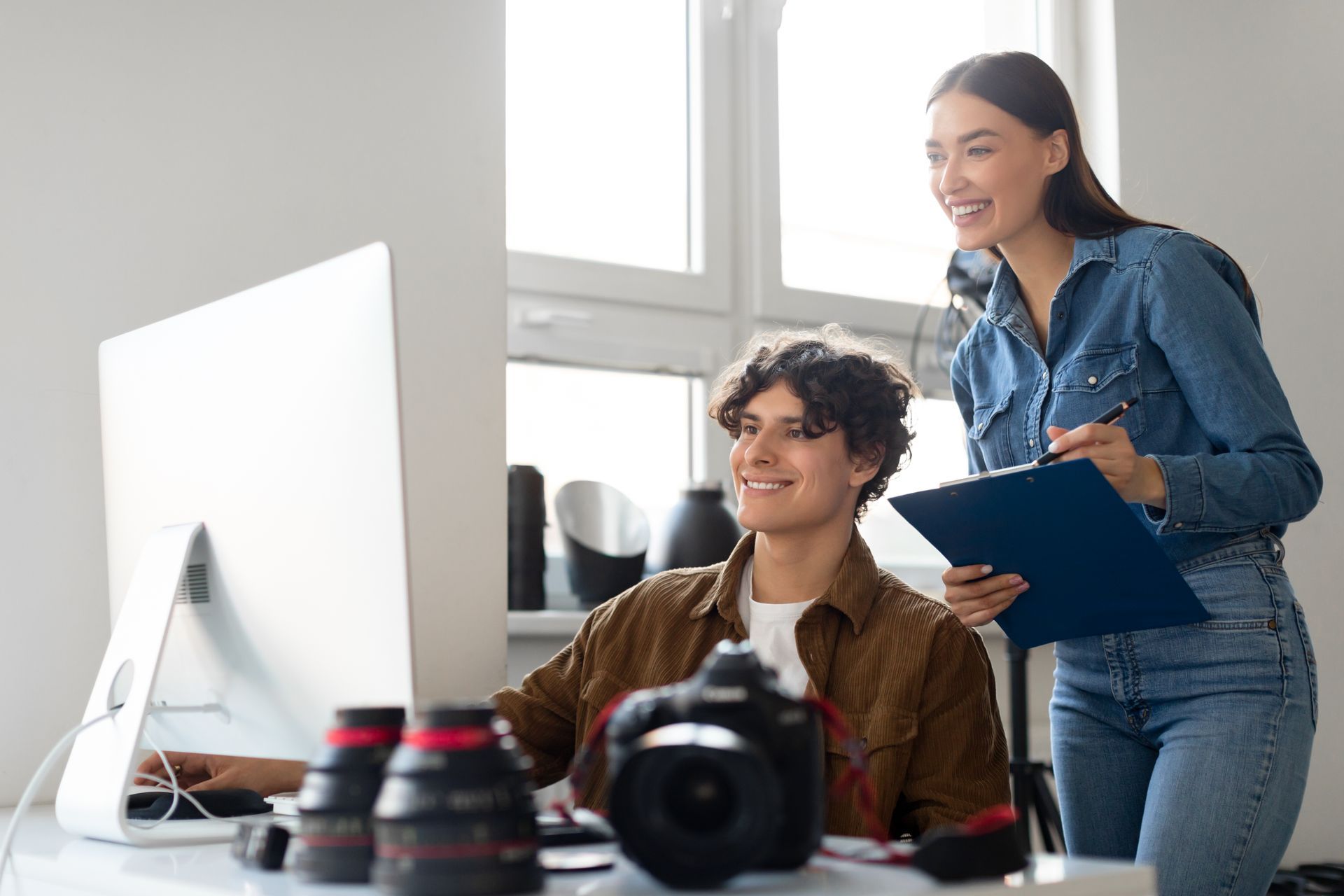 Happy professional team of photographer and assistant looking at computer monitor, transfering